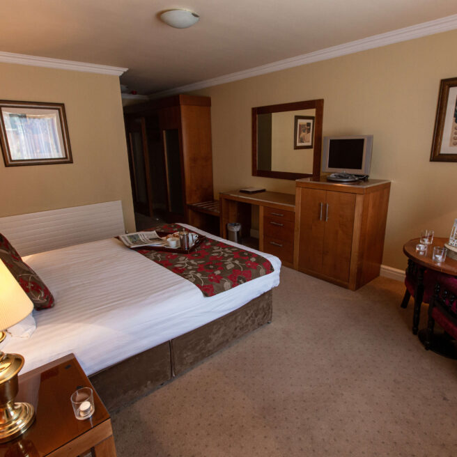 Elegant hotel room with king bed, warm lighting, cosy seating, and vibrant flowers.