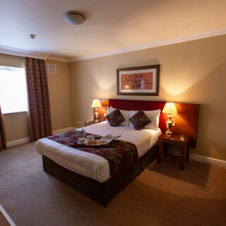 Cosy hotel room with warm lighting, double bed, and a breakfast tray on the bed at Hamlet Court Hotel.