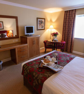 Elegant hotel room with cosy decor, a tray of breakfast on the bed, and warm lighting.