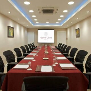 Elegant meeting room at Hamlet Court Hotel with a long table, chairs, and a projection screen.