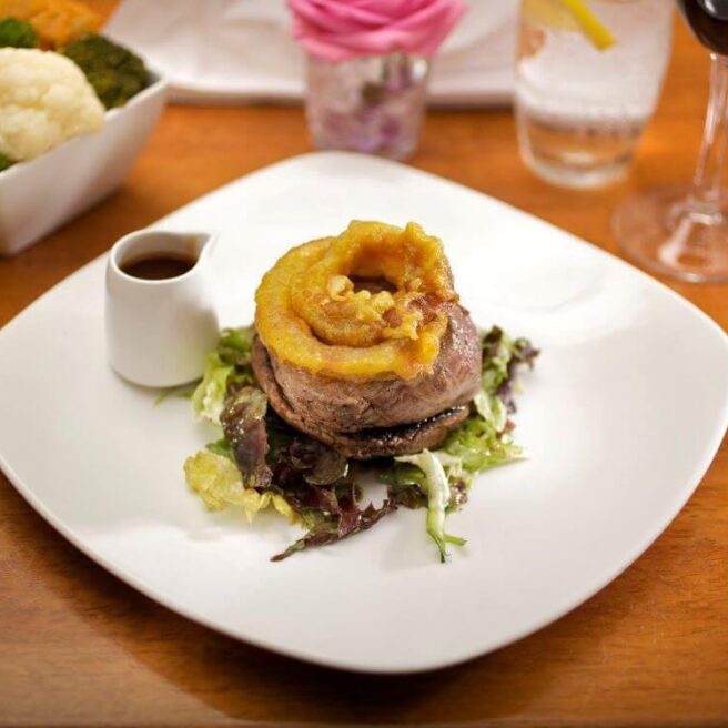 Gourmet meal on elegant plate at Hamlet Court Hotel, set with cutlery and drink nearby.