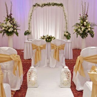 Elegant wedding venue with floral arch and white chairs adorned with gold sashes at Hamlet Court Hotel.