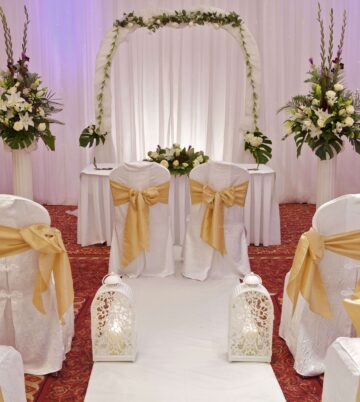 Elegant wedding venue with floral arch and white chairs adorned with gold sashes at Hamlet Court Hotel.