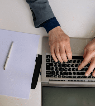Person typing on a laptop at a desk with white papers.