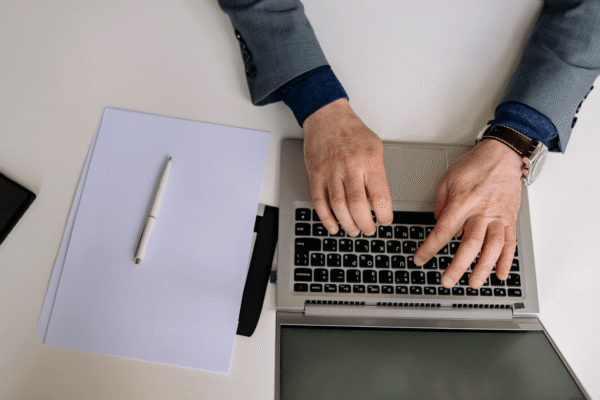 Person typing on a laptop at a desk with white papers.