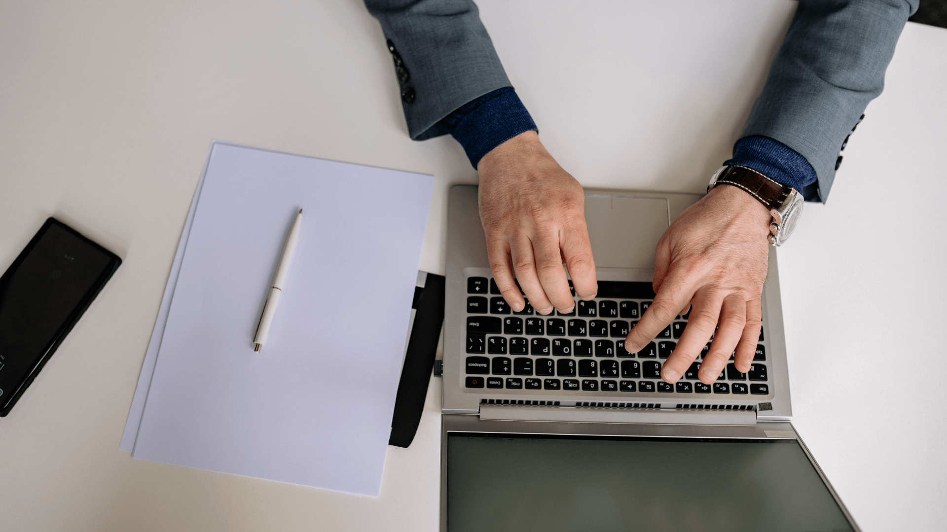Person typing on a laptop at a desk with white papers.