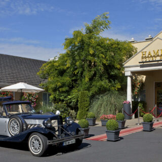 Classic car outside welcoming Hamlet Court Hotel with elegant entrance and lush landscaping.