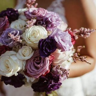 Bride holding a vibrant bouquet of roses and lilacs outdoors at Hamlet Court Hotel.