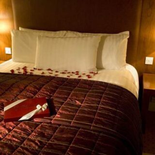 Cosy hotel room with a plush bed, warm lighting, and rose petals for a romantic atmosphere.