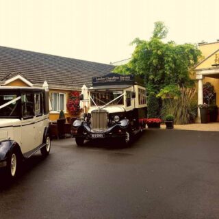 Charming Hamlet Court Hotel entrance with vintage cars on a serene, overcast day.