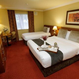 Cosy hotel room with twin and double beds, decorated warmly with soft lighting and artwork.