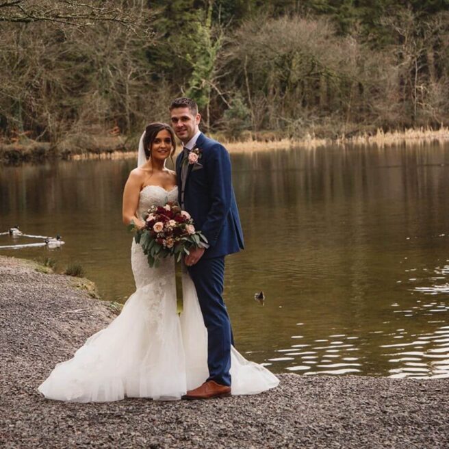 A cosy wedding by a serene lake at Hamlet Court Hotel. Bride and groom stand by the water.