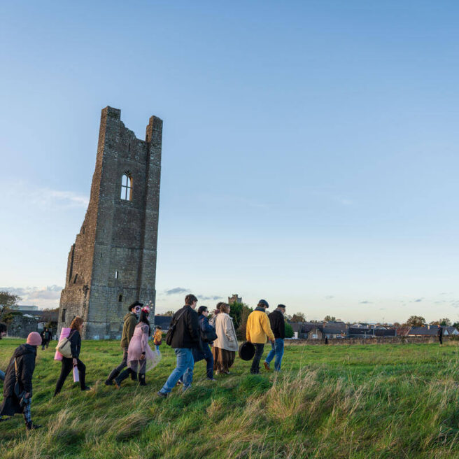 People walking towards an ancient tower under a clear blue sky at dusk.