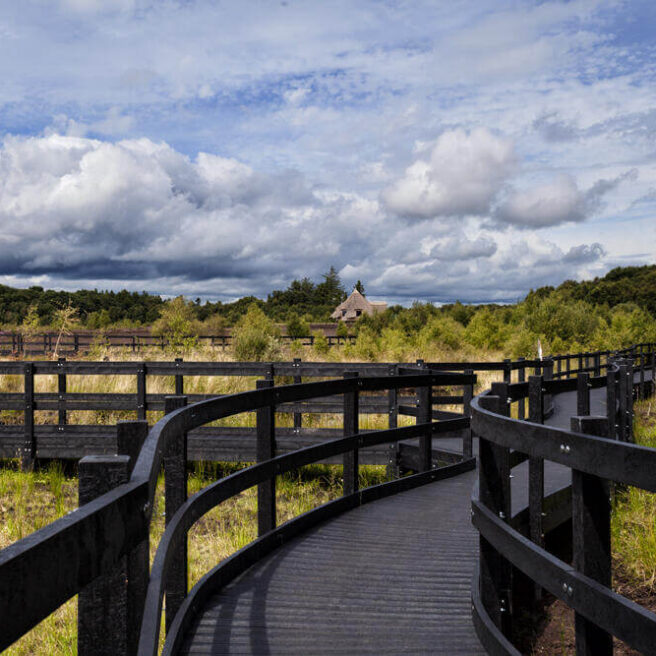 Wooden walkway through lush greenery under a partly cloudy sky at Hamlet Court Hotel.