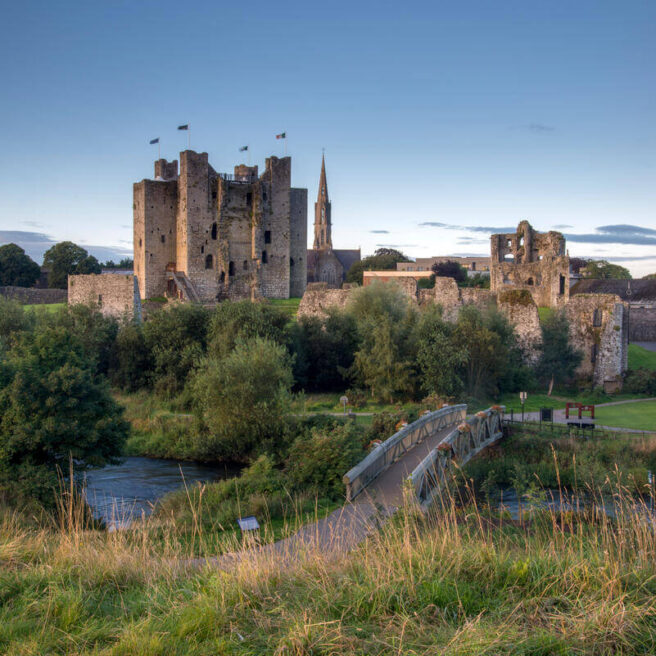 Historic stone castle with lush greenery and river in serene countryside setting.